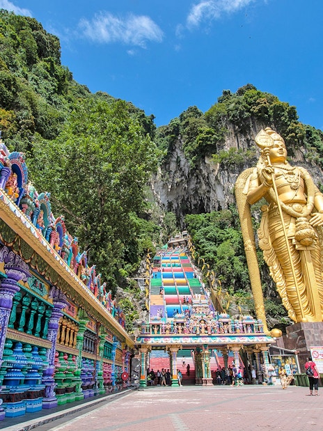 Batu Caves entrance with colorful steps and large golden statue in Kuala Lumpur.