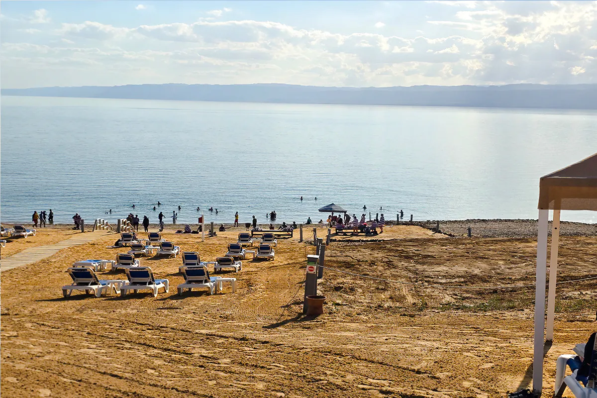 Beachgoers floating in the Dead Sea near Amman with sun loungers on the sandy shore.