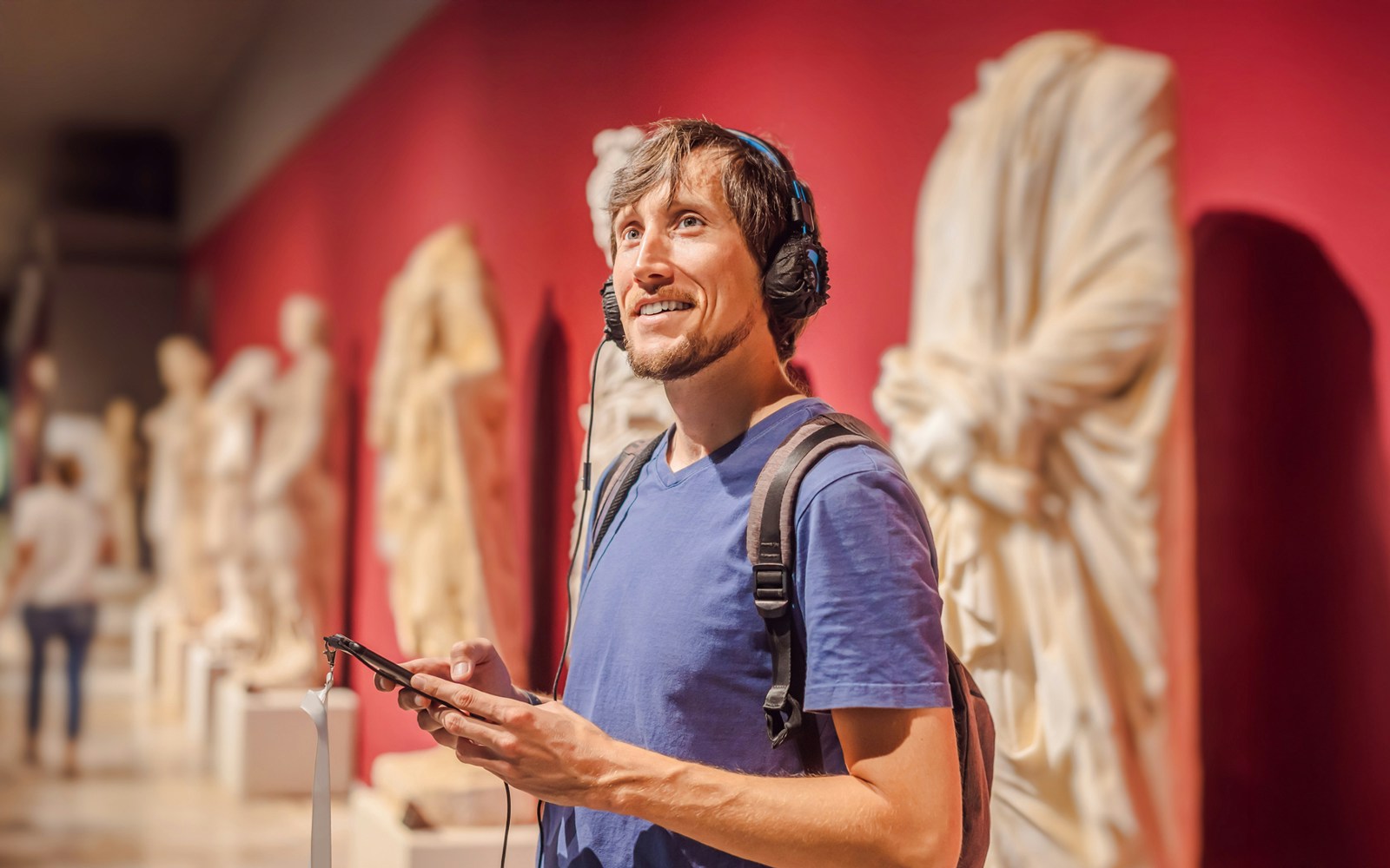 Man with headphones using audio guide in museum sculpture gallery.