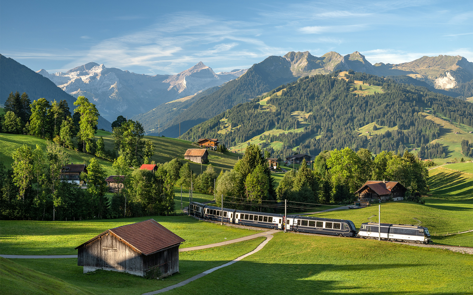 GoldenPass Express train traveling through scenic Schönried with mountain backdrop.