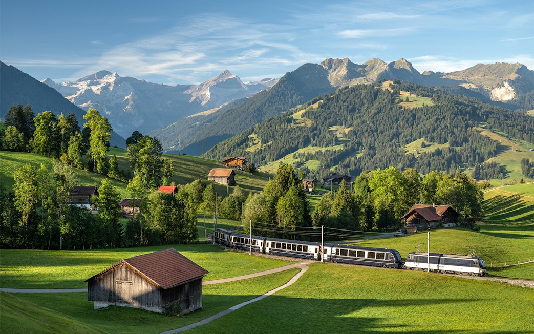 GoldenPass Express train traveling through scenic Schönried with mountain backdrop.