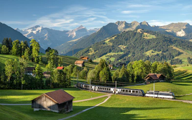 GoldenPass Express train traveling through scenic Schönried with mountain backdrop.
