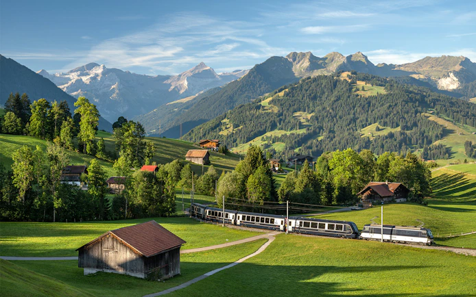 GoldenPass Express train traveling through scenic Schönried with mountain backdrop.