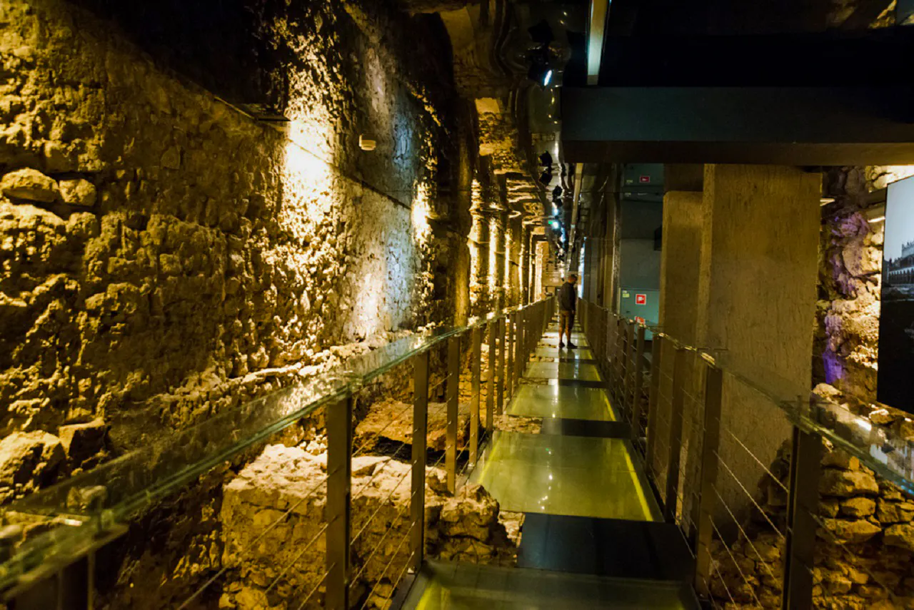 Underground passage in Krakow's museum with ancient stone walls and illuminated walkway.