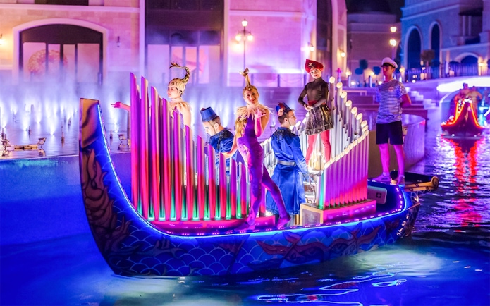 Performers in colorful costumes on a lit boat during The Land of Legends boat parade.