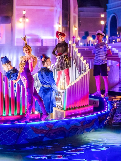 Performers in colorful costumes on a lit boat during The Land of Legends boat parade.