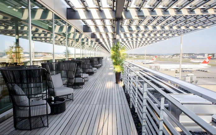 Outdoor seating area at Primeclass Lounge, Zurich Airport Terminal E, overlooking runway.