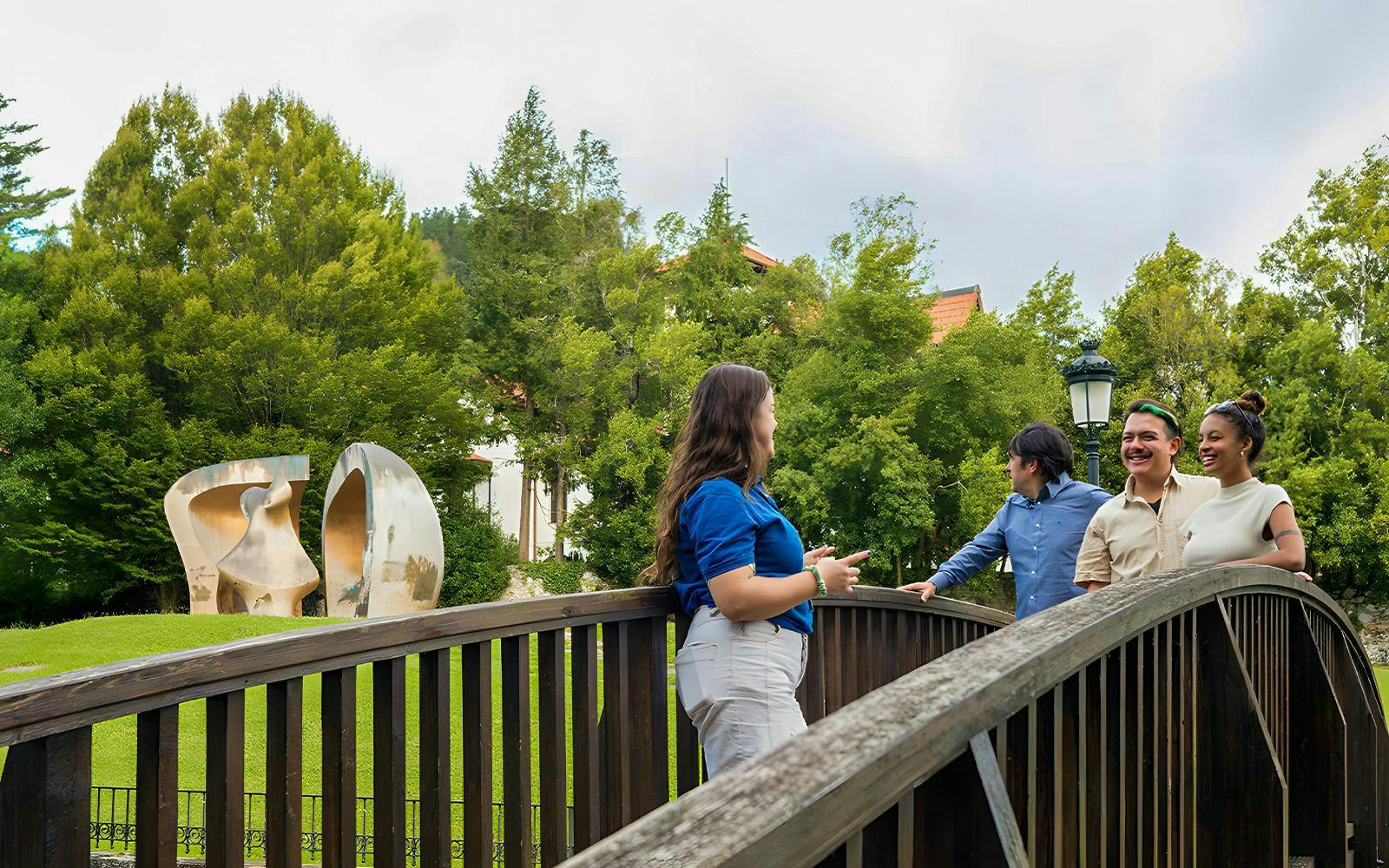 Tourists with guide on a bridge near Guernica sculpture in a park setting.