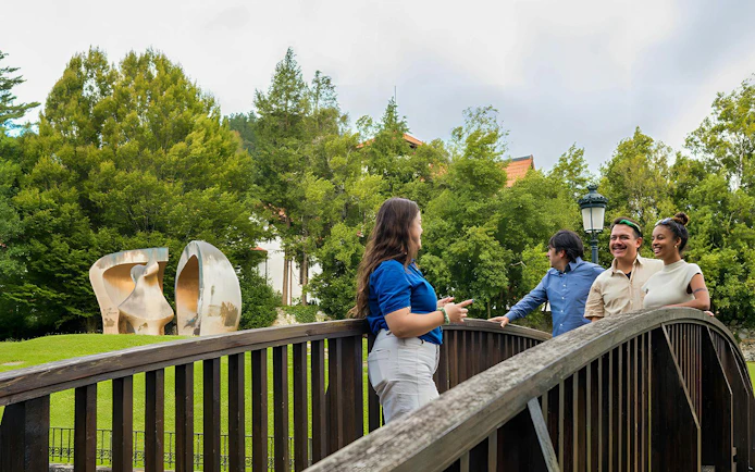 Tourists with guide on a bridge near Guernica sculpture in a park setting.