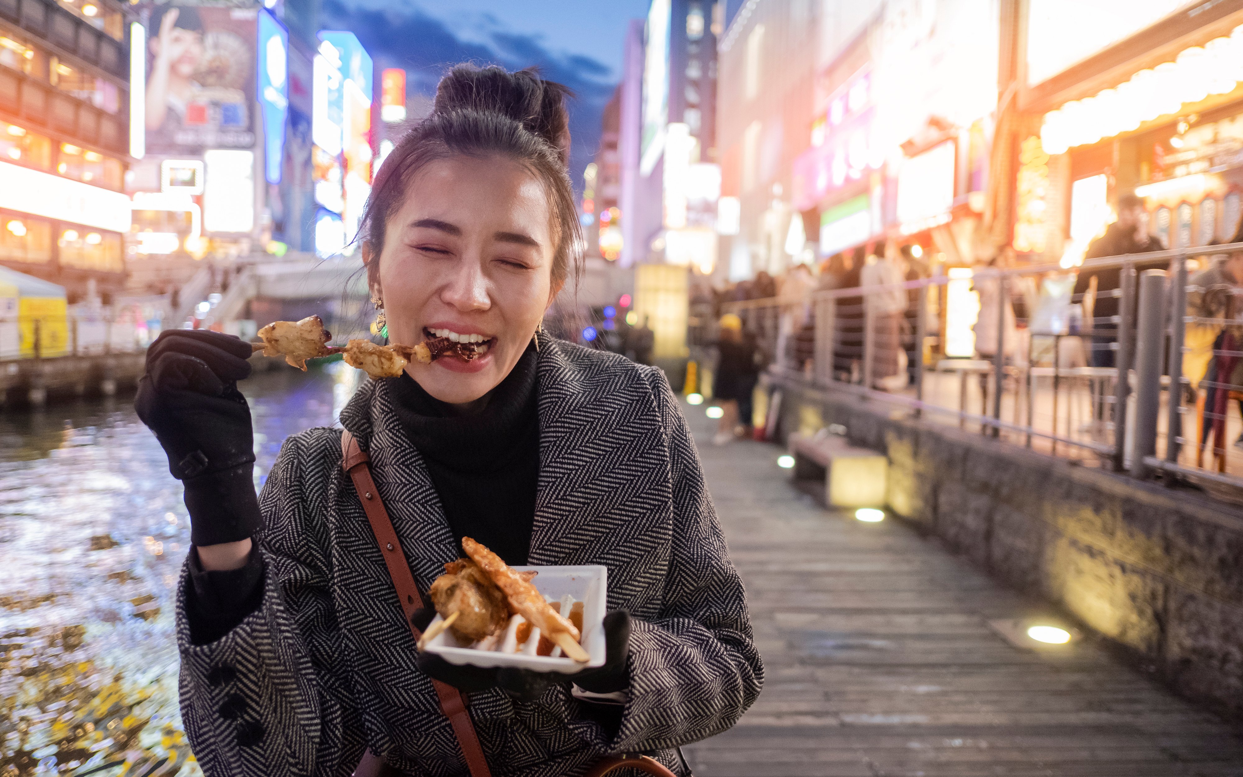 Young woman eating street food at Dotonbori shopping center, Osaka, Japan.