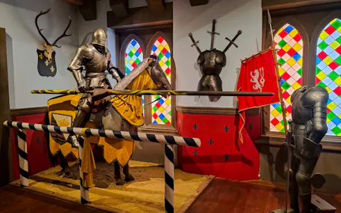 Knight armor display at Story of Prague Museum, featuring medieval jousting scene with colorful stained glass.