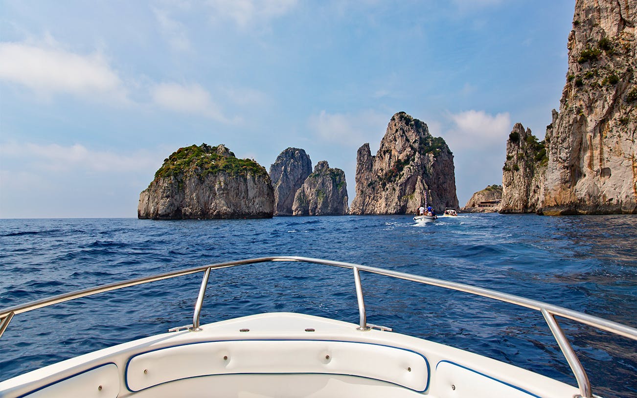 Boat approaching Faraglioni rocks on Capri tour from Rome.