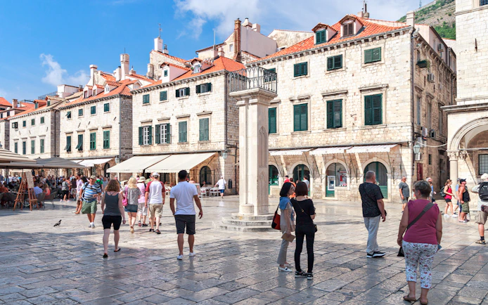 Tourists exploring Dubrovnik's historic square with stone buildings and a column, Walls & Wars Tour.