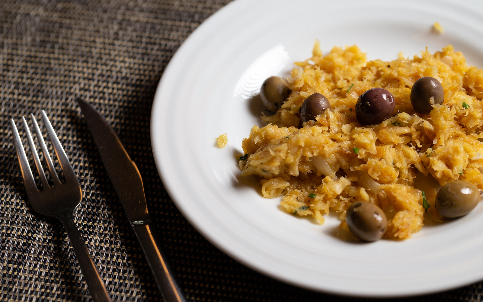 Bacalhau à Brás with olives on a white plate, Portuguese cuisine.