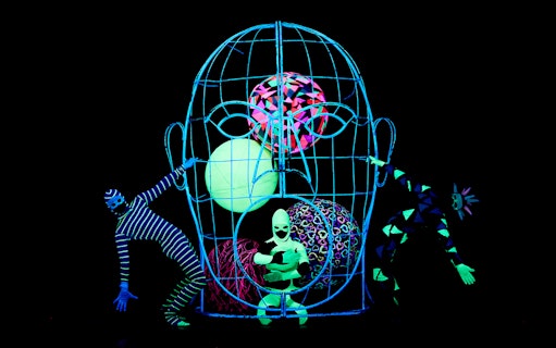 Black Light Theater performers in neon costumes with abstract props, Prague.