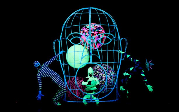 Black Light Theater performers in neon costumes with abstract props, Prague.