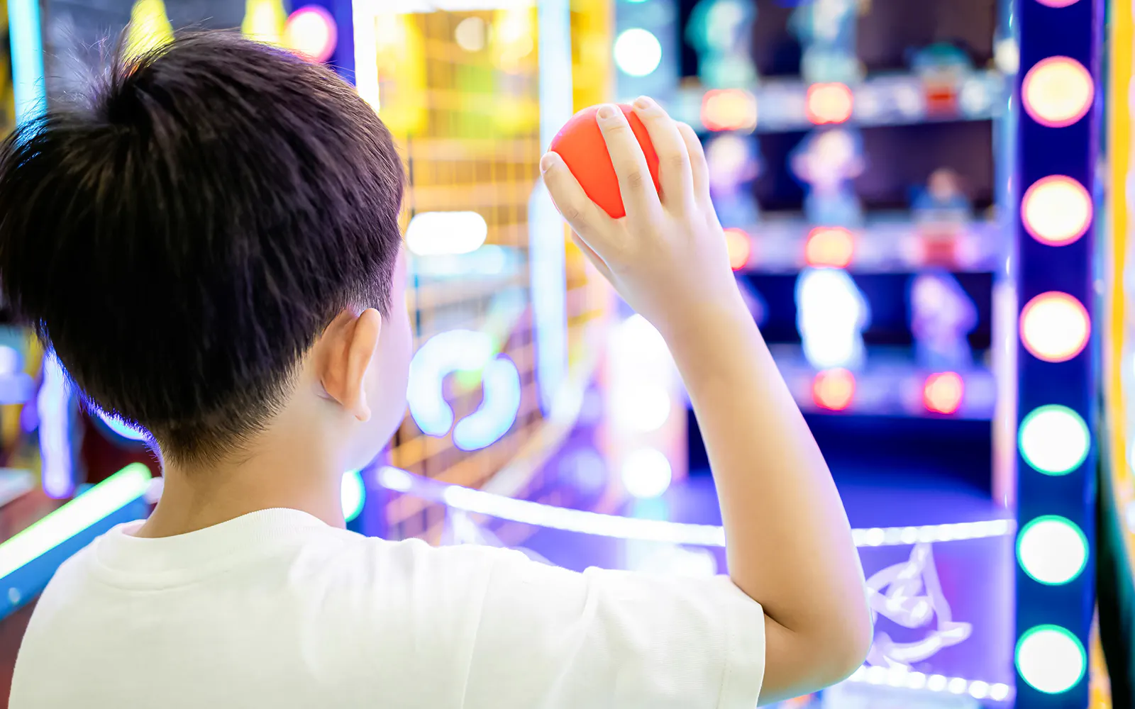 Child aiming a plastic ball at arcade targets.
