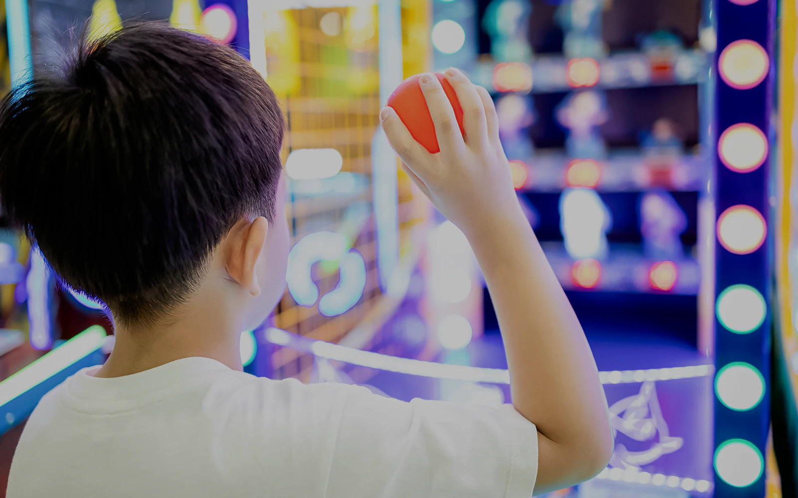 Child aiming a plastic ball at arcade targets.
