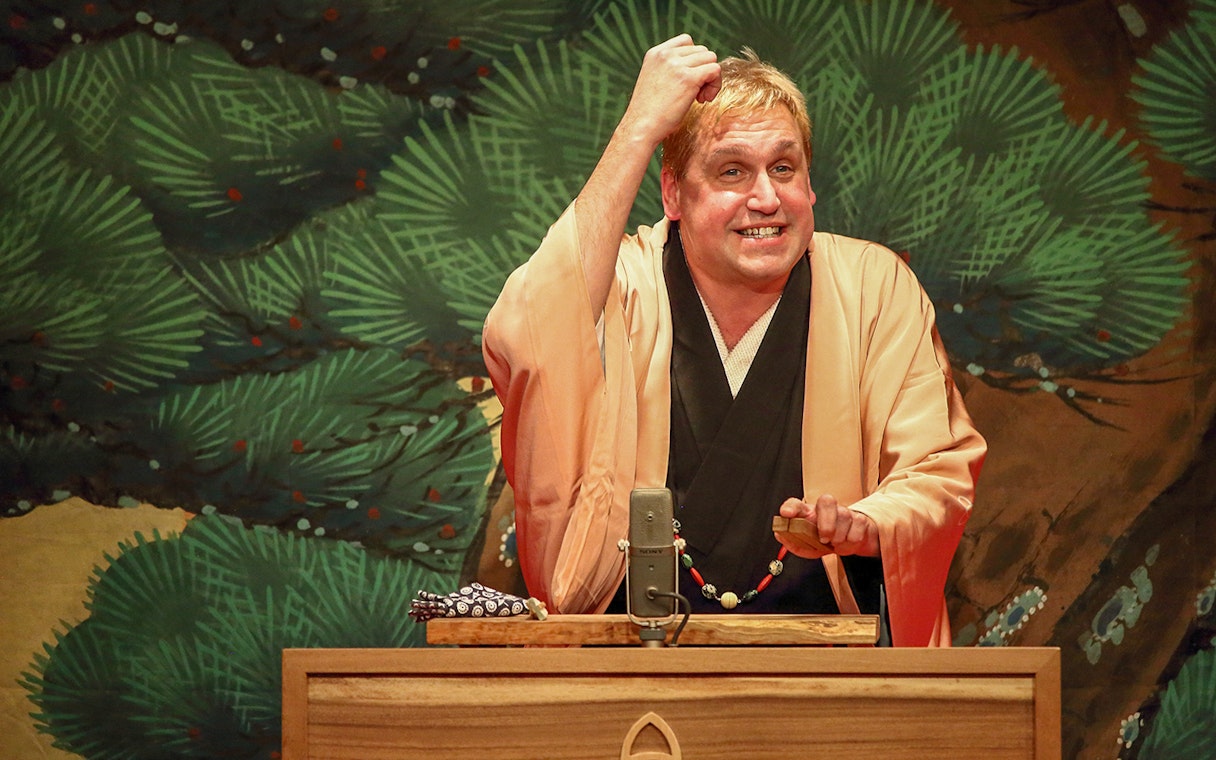 Rakugo performer on stage with traditional backdrop.