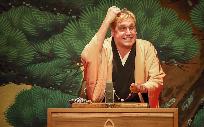 Rakugo performer on stage with traditional backdrop.