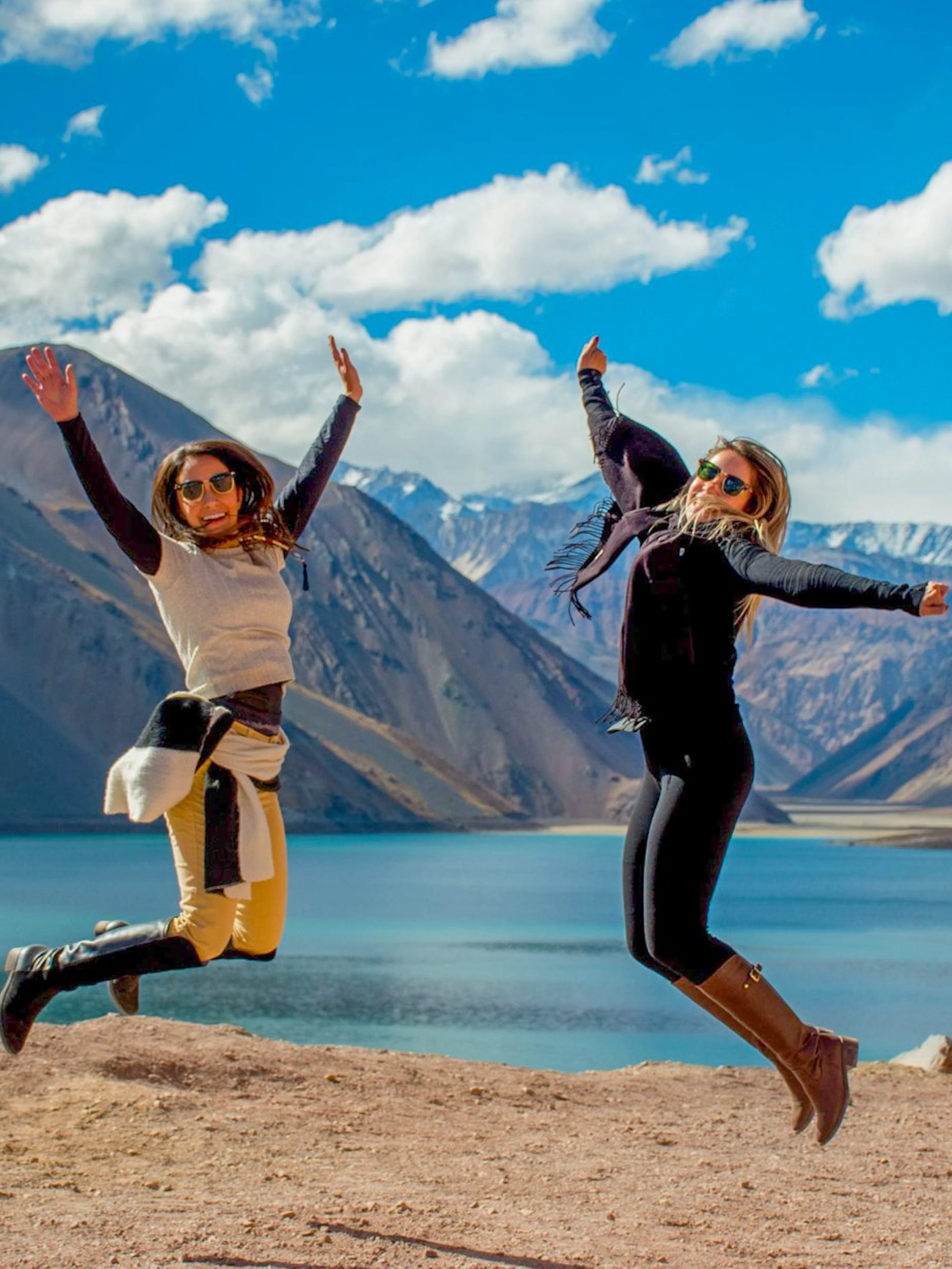 Two people jumping at El Yeso Reservoir in the Andes Mountains, Chile.