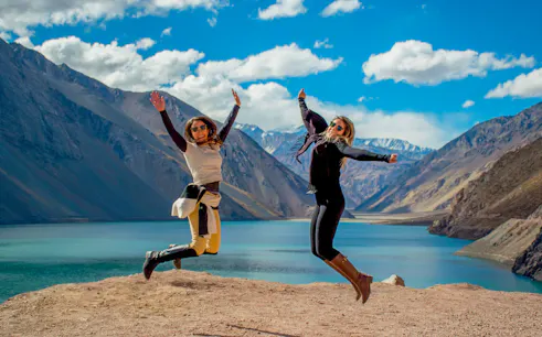 Two people jumping at El Yeso Reservoir in the Andes Mountains, Chile.