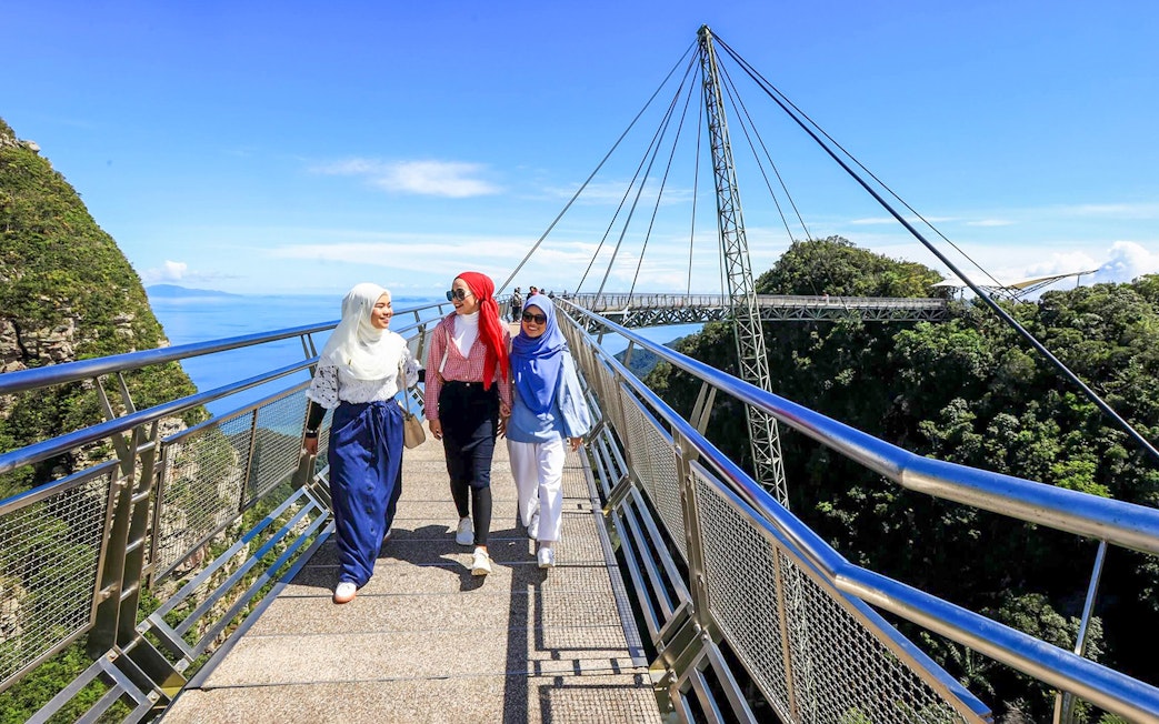 Women walking on Langkawi Sky Bridge with scenic views of the forest and ocean.