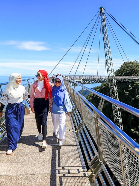 Women walking on Langkawi Sky Bridge with scenic views of the forest and ocean.