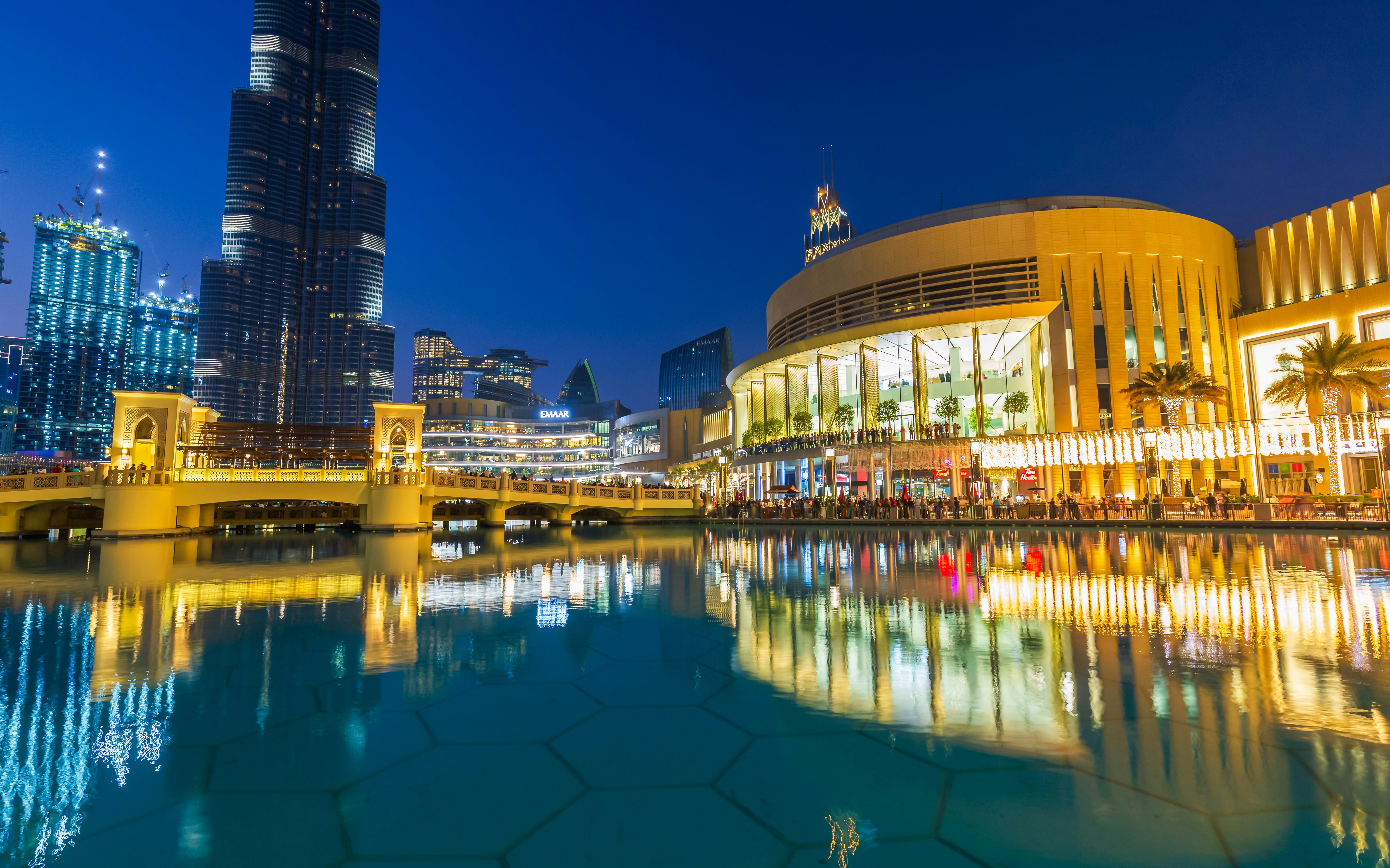 Dubai Mall's modern architecture and luxury shops reflected in the fountain at night.