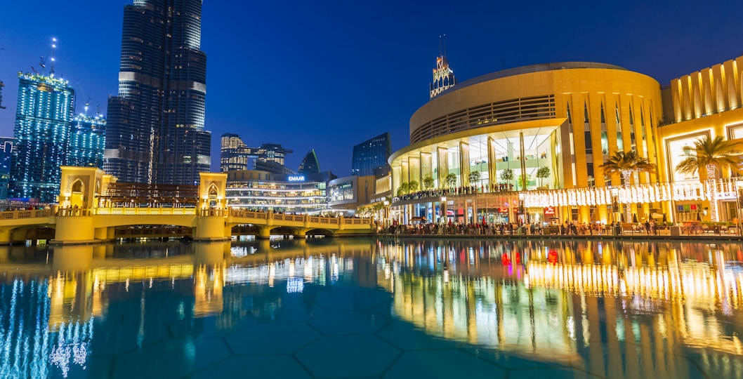 Dubai Mall's modern architecture and luxury shops reflected in the fountain at night.
