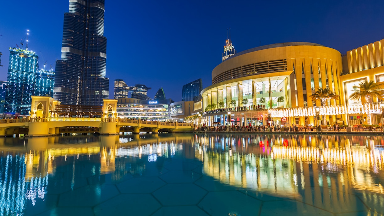 Dubai Mall's modern architecture and luxury shops reflected in the fountain at night.