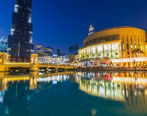 Dubai Mall's modern architecture and luxury shops reflected in the fountain at night.
