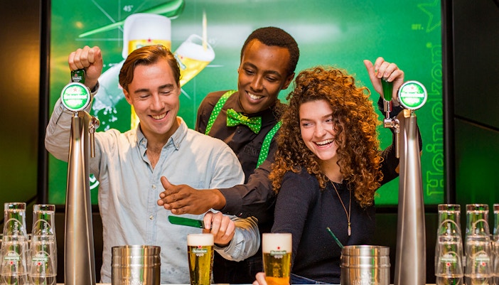 Visitors exploring Heineken brewery in Amsterdam with drinks in hand.