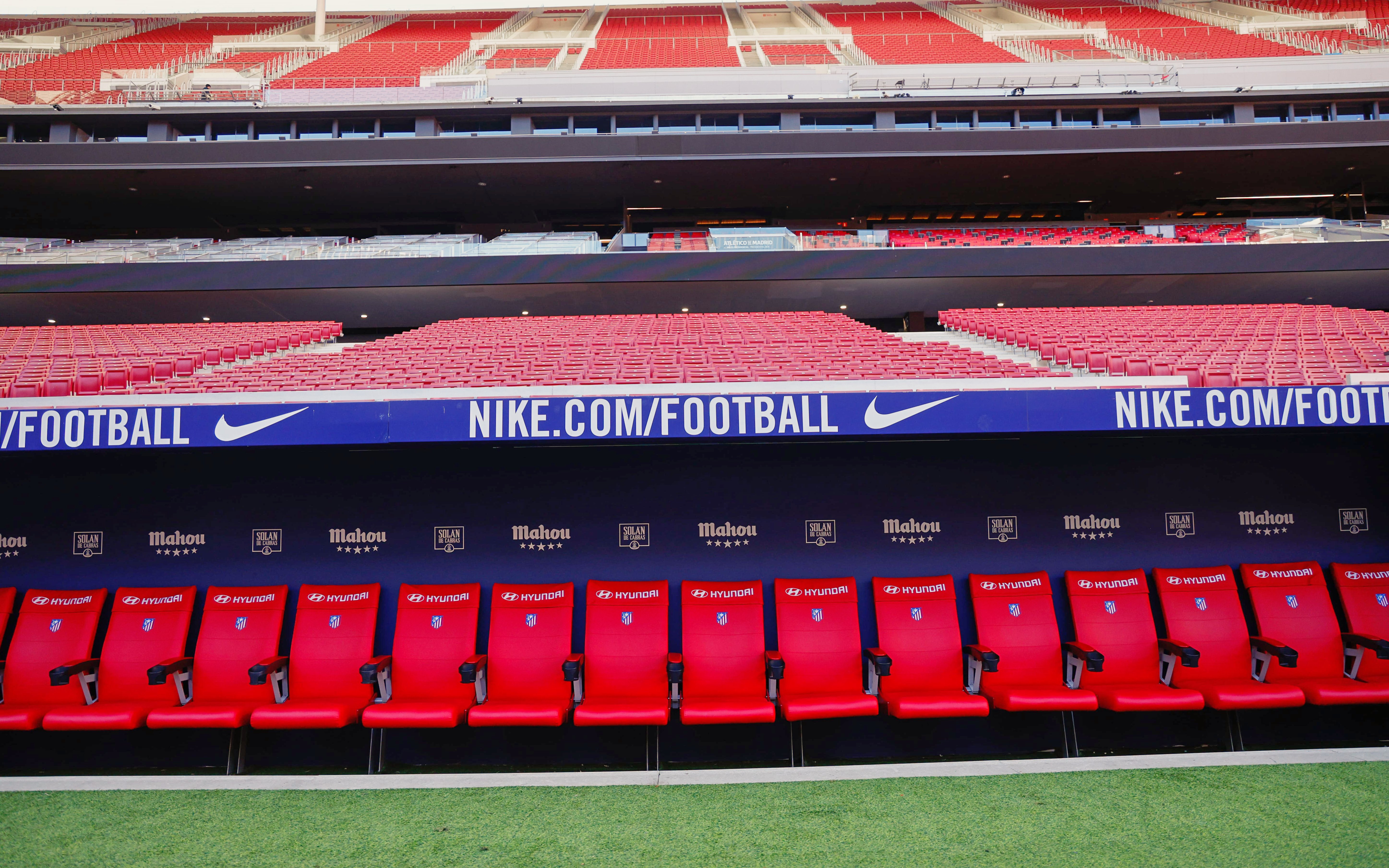 Players seating area at Atletico de Madrid Stadium with red seats and sponsor logos.