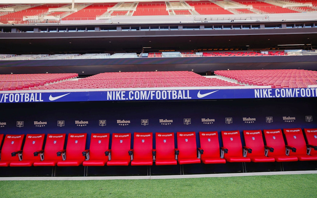Players seating area at Atletico de Madrid Stadium with red seats and sponsor logos.