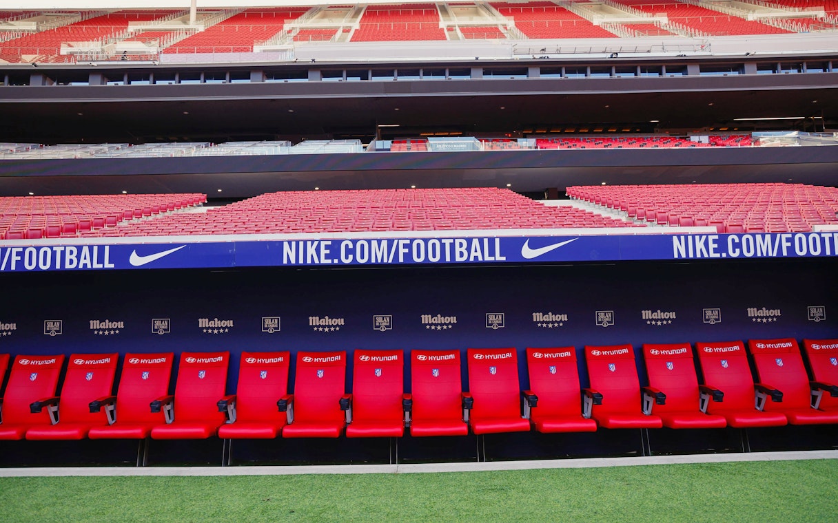 Players seating area at Atletico de Madrid Stadium with red seats and sponsor logos.