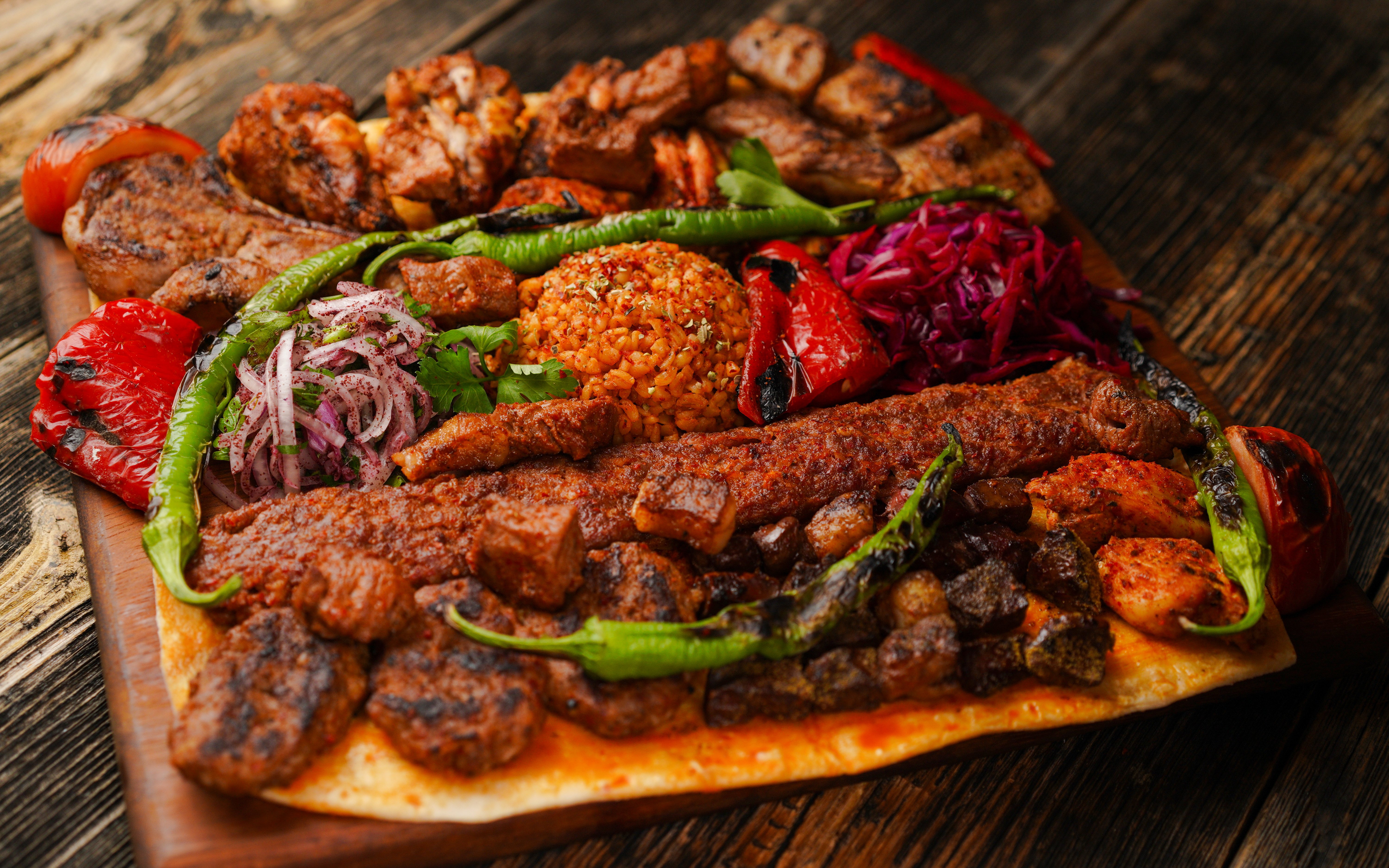 Assorted Turkish grills with kebabs, grilled vegetables, and bulgur on a wooden platter.