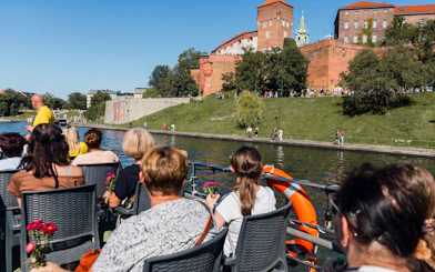 Tourists on a river cruise in Krakow with Wawel Castle in the background.