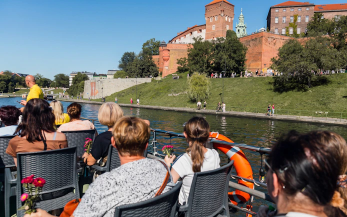 Tourists on a river cruise in Krakow with Wawel Castle in the background.