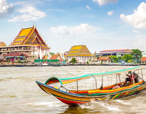 Traditional long-tail boat on Chao Phraya River with Bangkok temples in background.