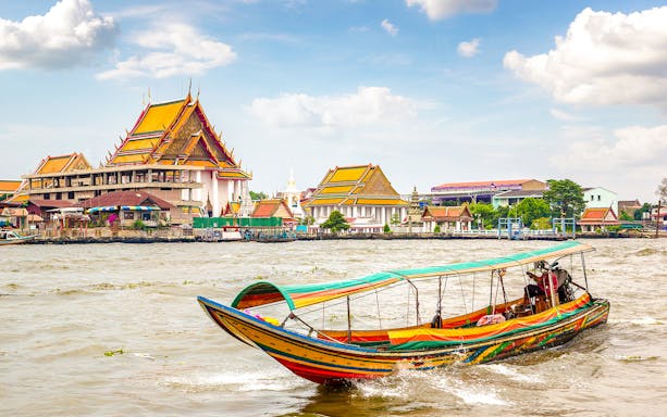 Traditional long-tail boat on Chao Phraya River with Bangkok temples in background.