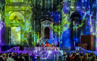 Orchestra performing in a historic Florence venue with colorful light projections.