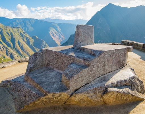 Ancient stone sundial at Machu Picchu with Andes Mountains in the background, Peru.