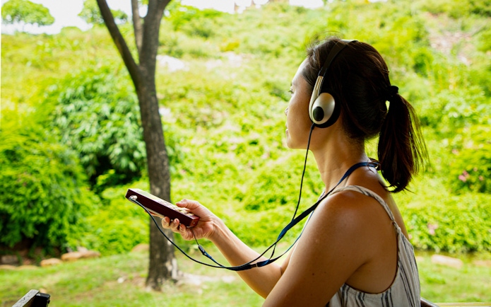 Tourist using audio guide in a lush green park setting.
