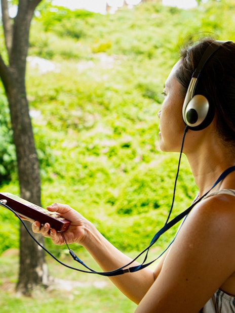 Tourist using audio guide in a lush green park setting.