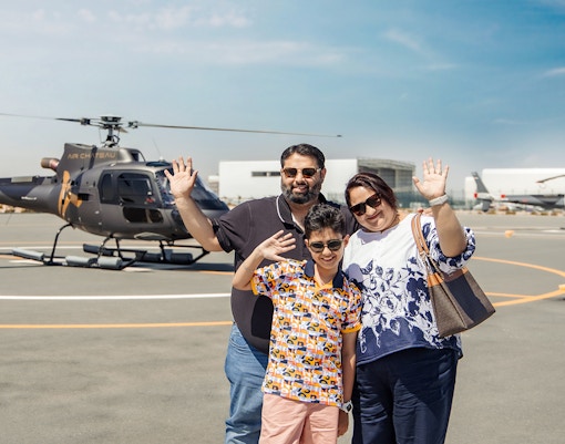 Family waving near helicopter on tarmac, ready for helicopter tour with return transfer.