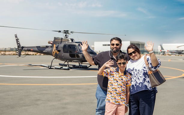 Family waving near helicopter on tarmac, ready for helicopter tour with return transfer.