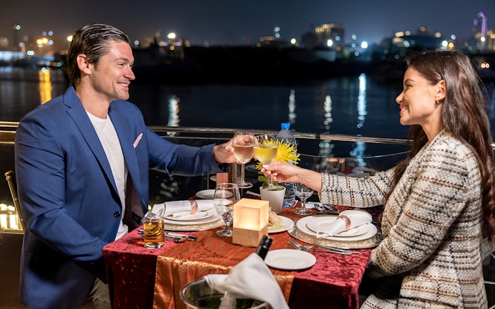 Couple toasting wine glasses on Luxury Dhow Cruise at night.