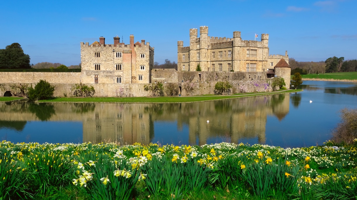 Leeds Castle reflected in a lake with blooming daffodils in the foreground.