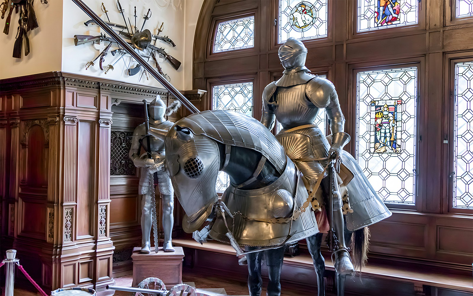 Knight armor display inside Peles Castle with stained glass windows.